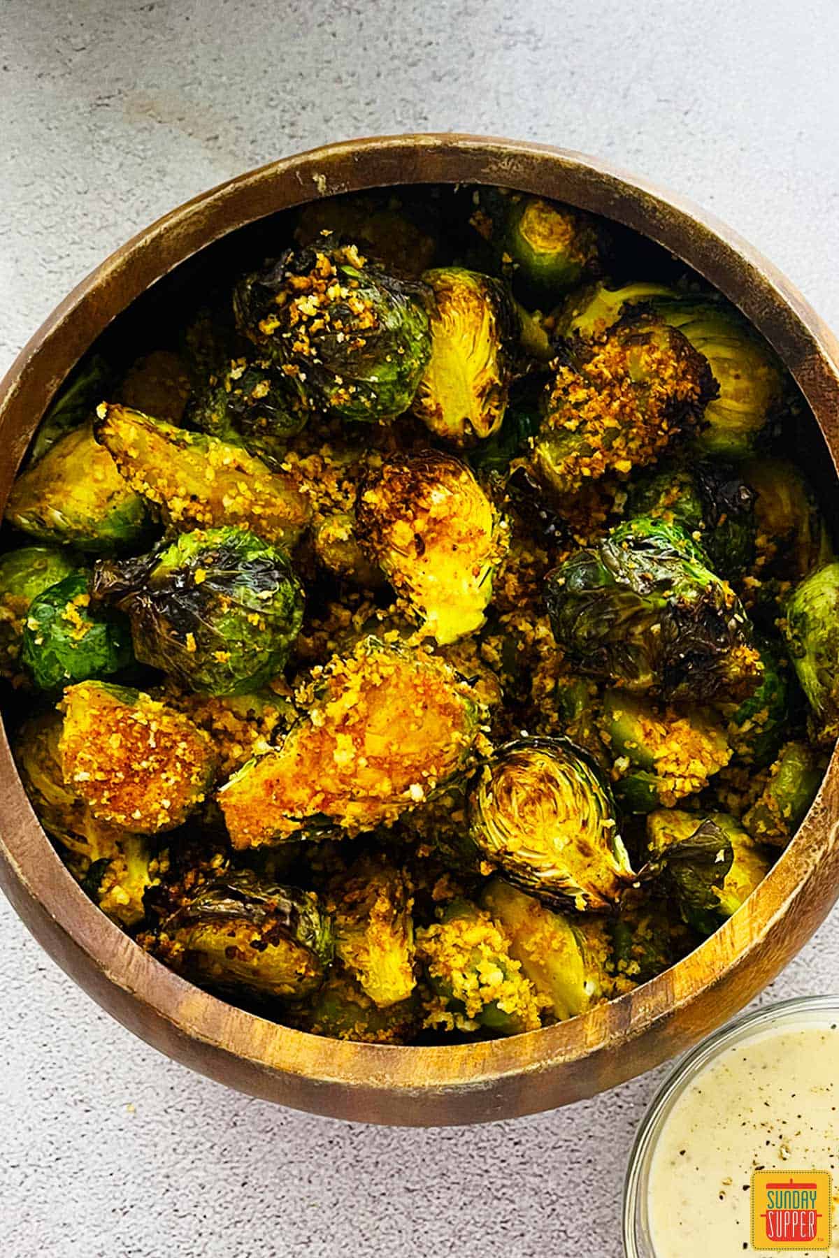 Air fried brussels sprouts in a wooden bowl next to dipping sauce