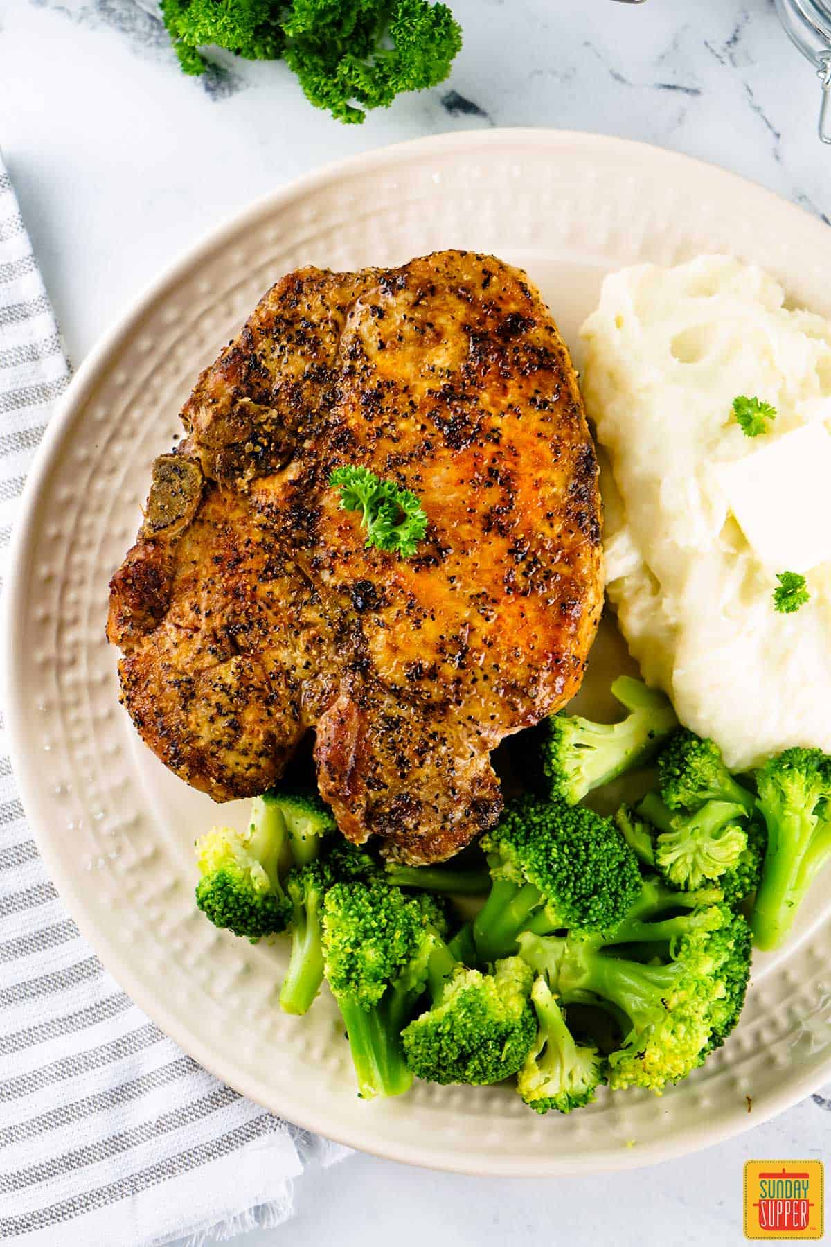 Grilled pork chop on a white plate with mashed potatoes and broccoli