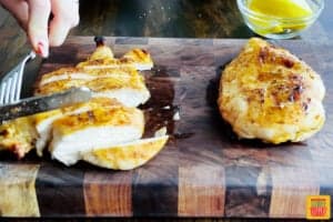 slicing grilled chicken breasts on a wood cutting board