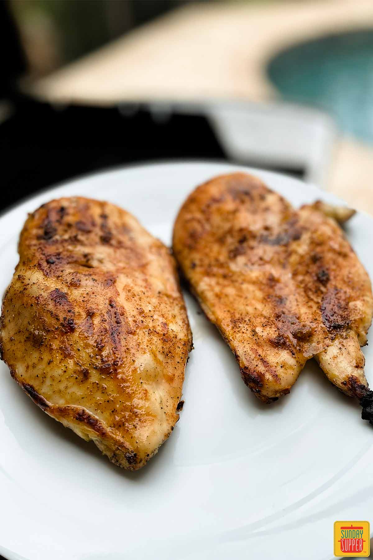 Two grilled chicken breasts on a white plate