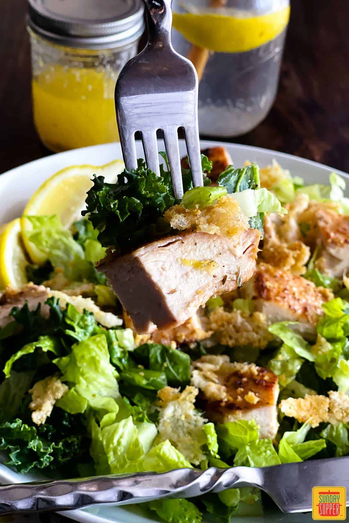 A fork with grilled chicken over kale caesar salad
