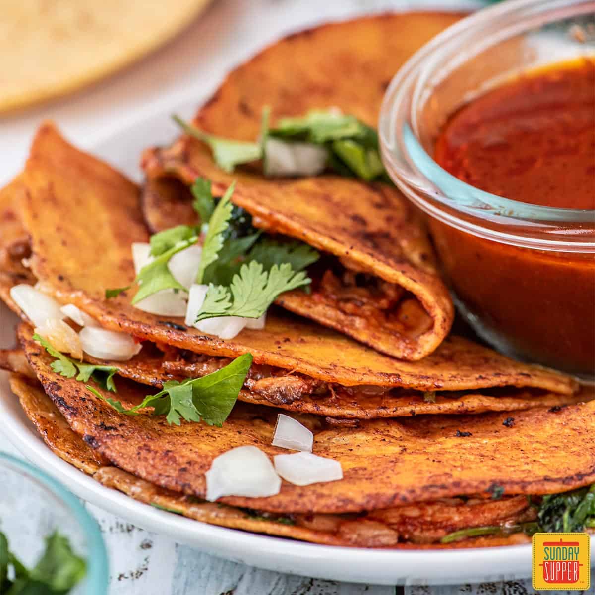 Three chicken birria tacos on a white plate with birria sauce on the side