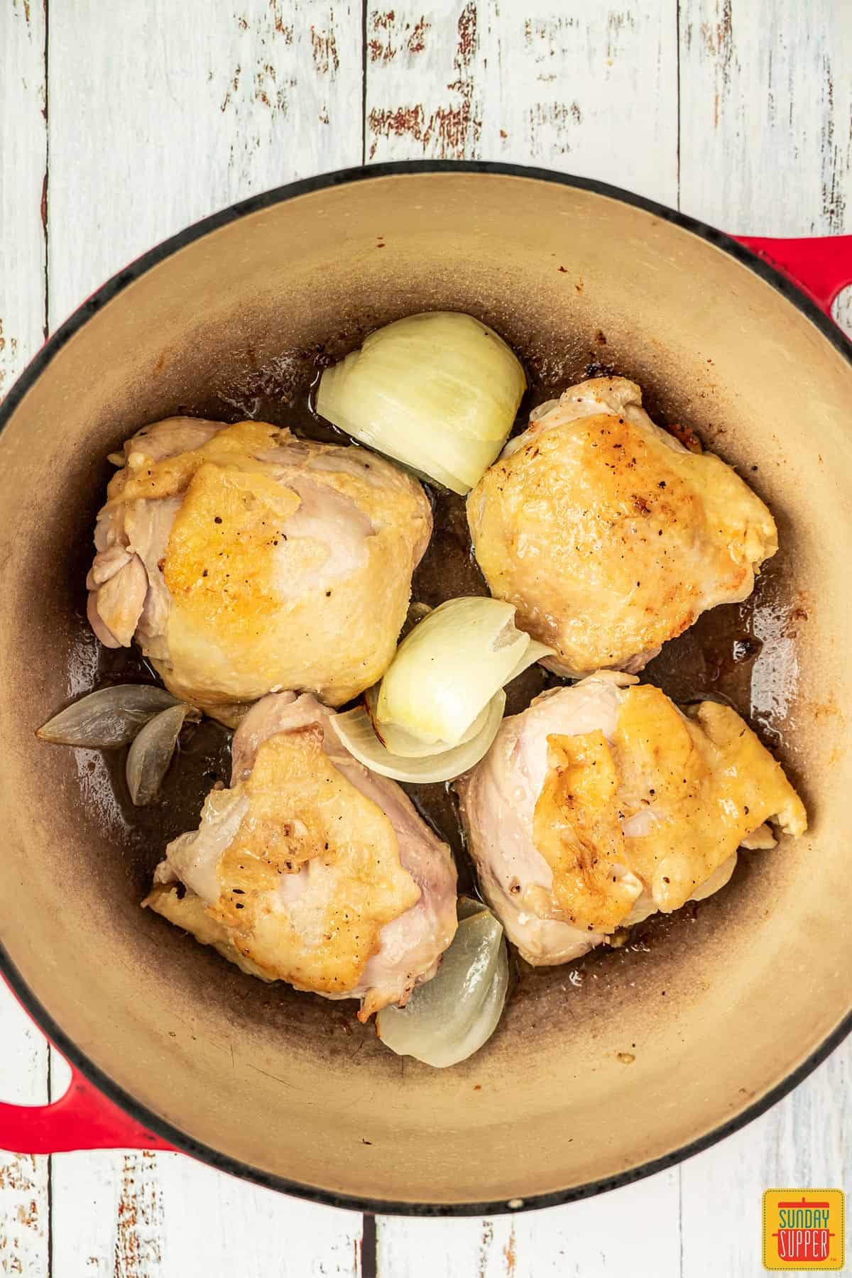 cooking chicken thighs in a pot with onions