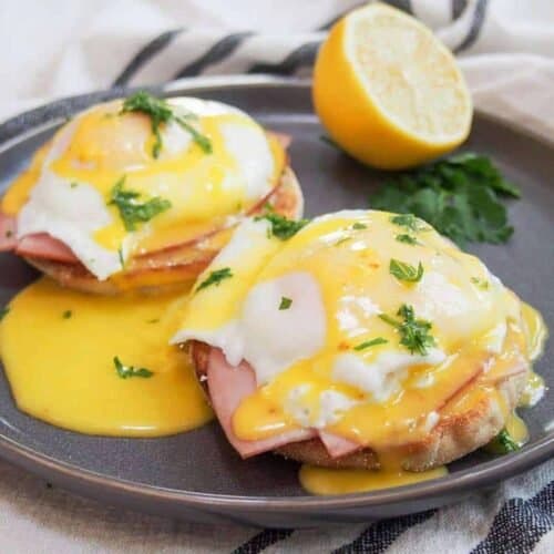 Eggs benedict on a black plate with fresh citrus