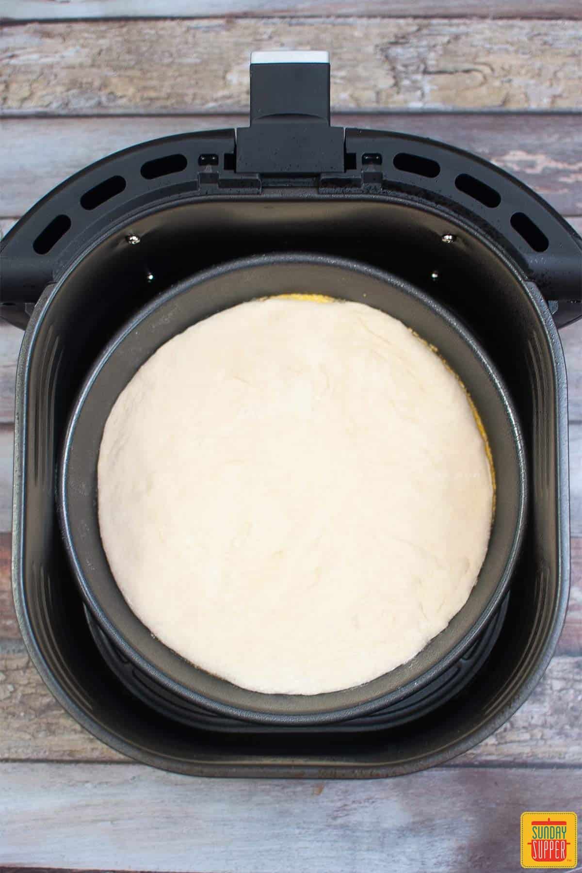 pizza dough flattened out in a pie pan in the air fryer