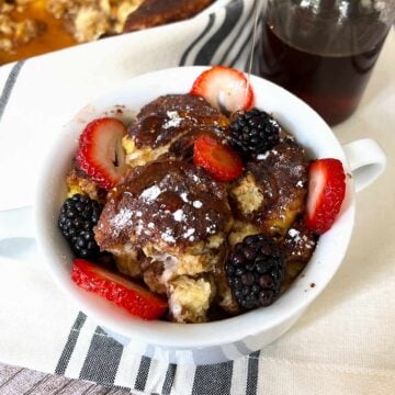 french toast casserole in a white mug with syrup and fruit