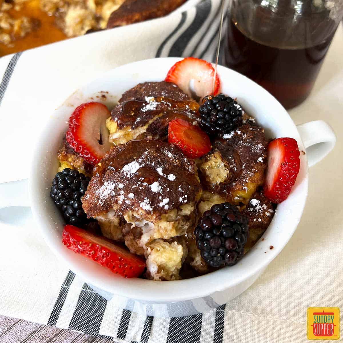french toast casserole in a white mug with syrup and fruit