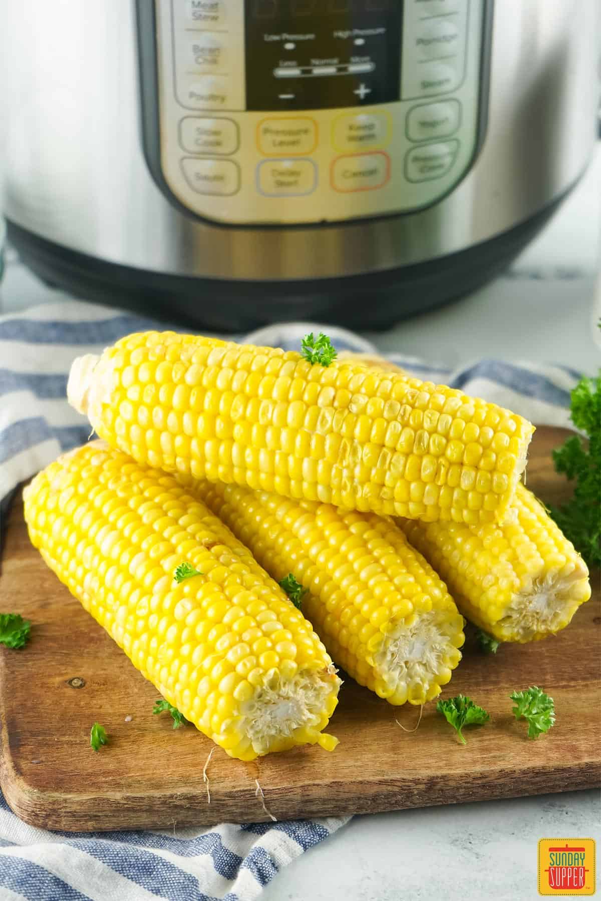 corn on the cob on a cutting board in front of an instant pot