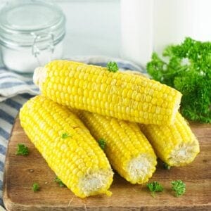 Four corn on the cob stacked on a cutting board
