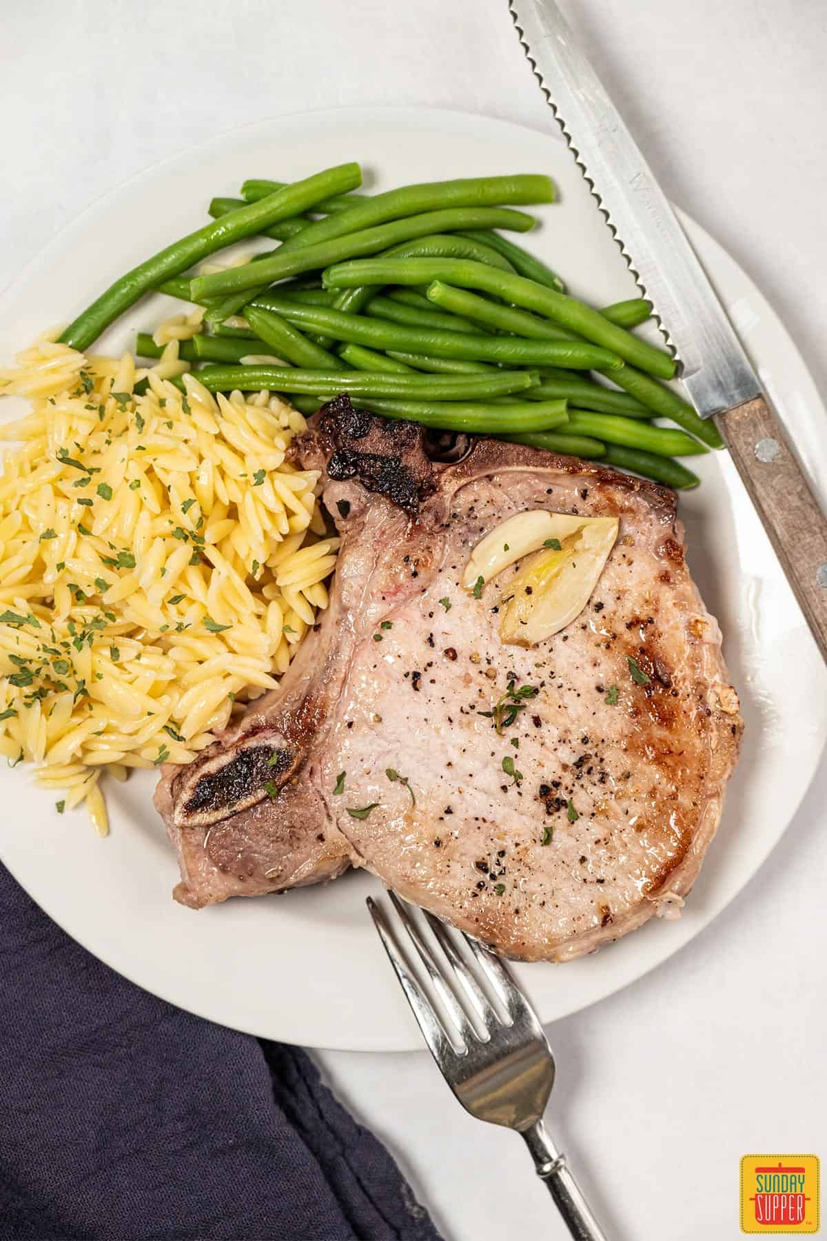 pork chops on a plate with orzo and green beans