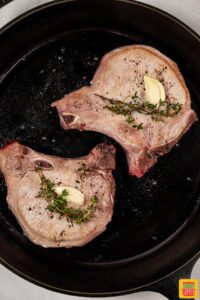 pork chops topped with thyme and garlic in pan