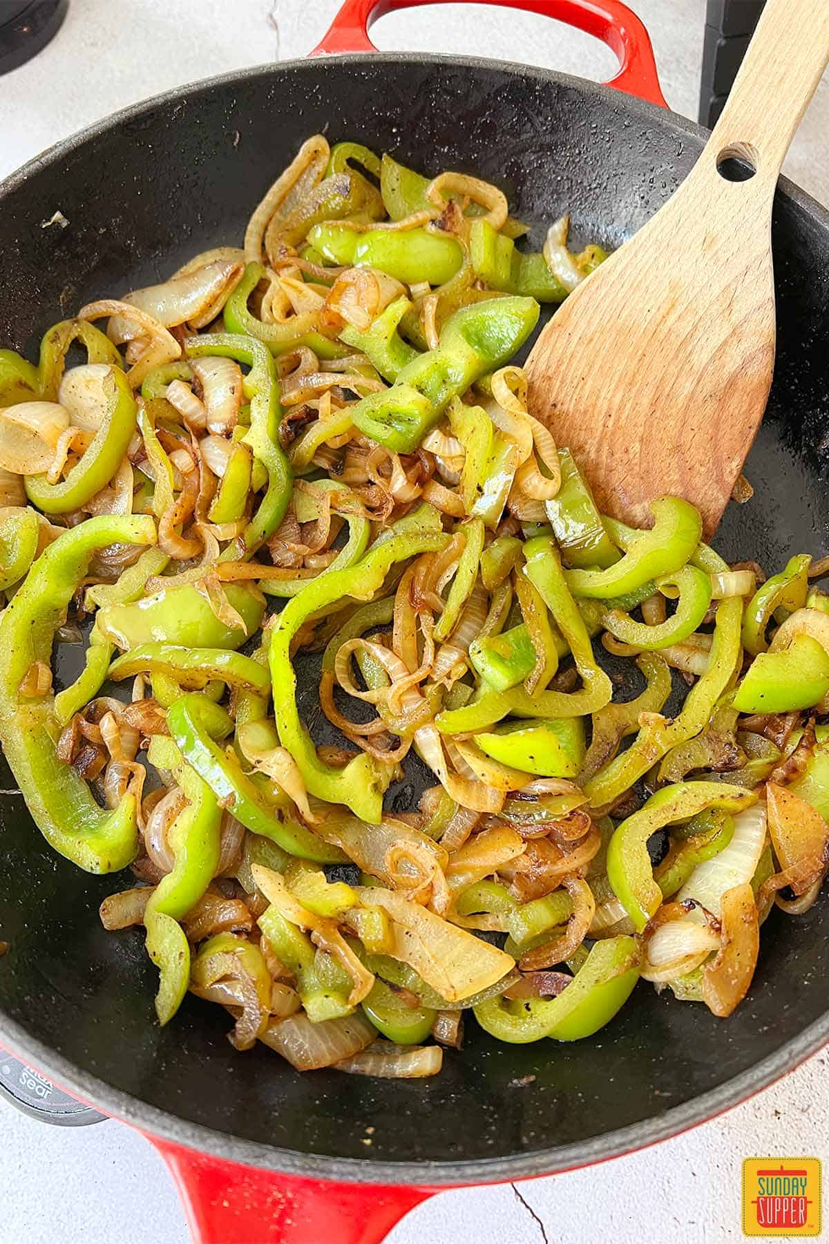 stirring peppers and onions in skillet with wooden spoon