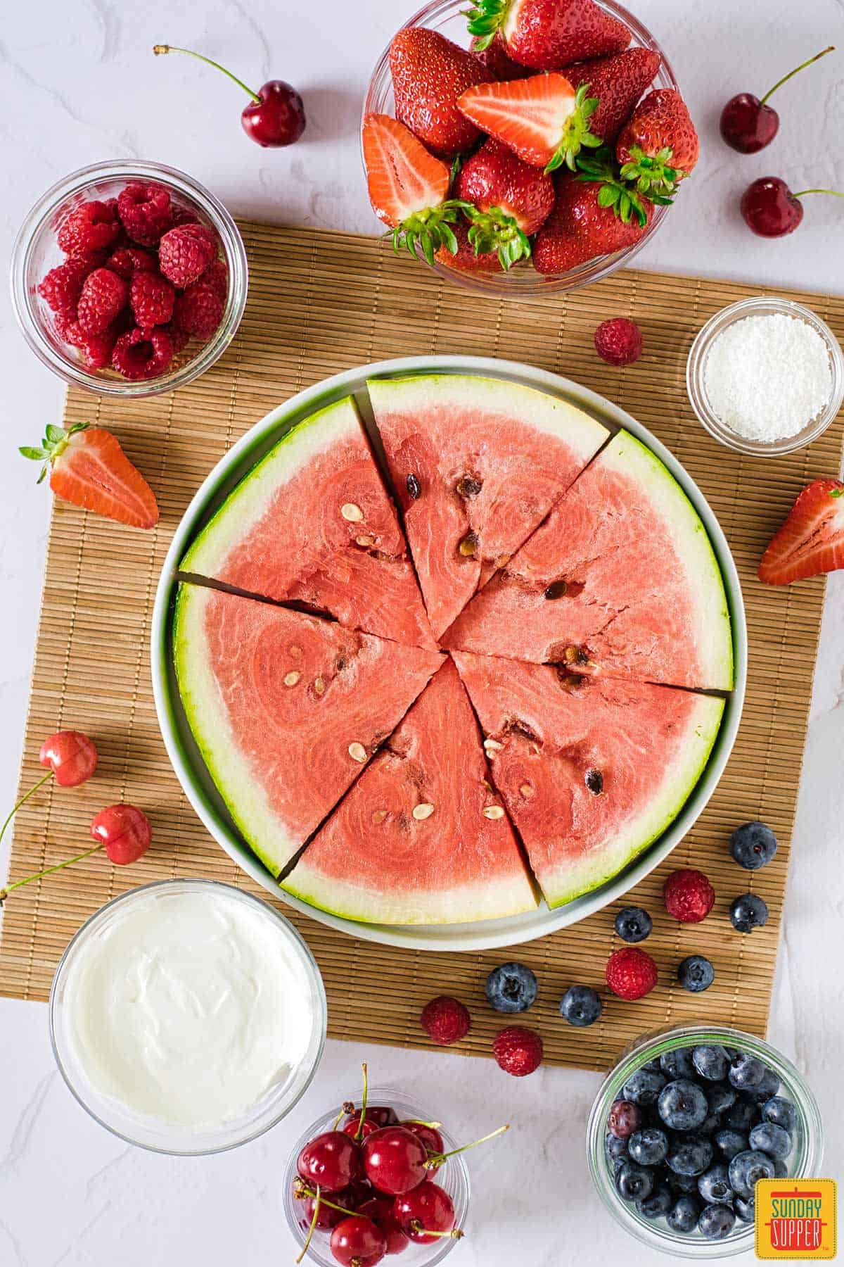 watermelon cut into slices next to a bowl of yogurt and fresh fruits