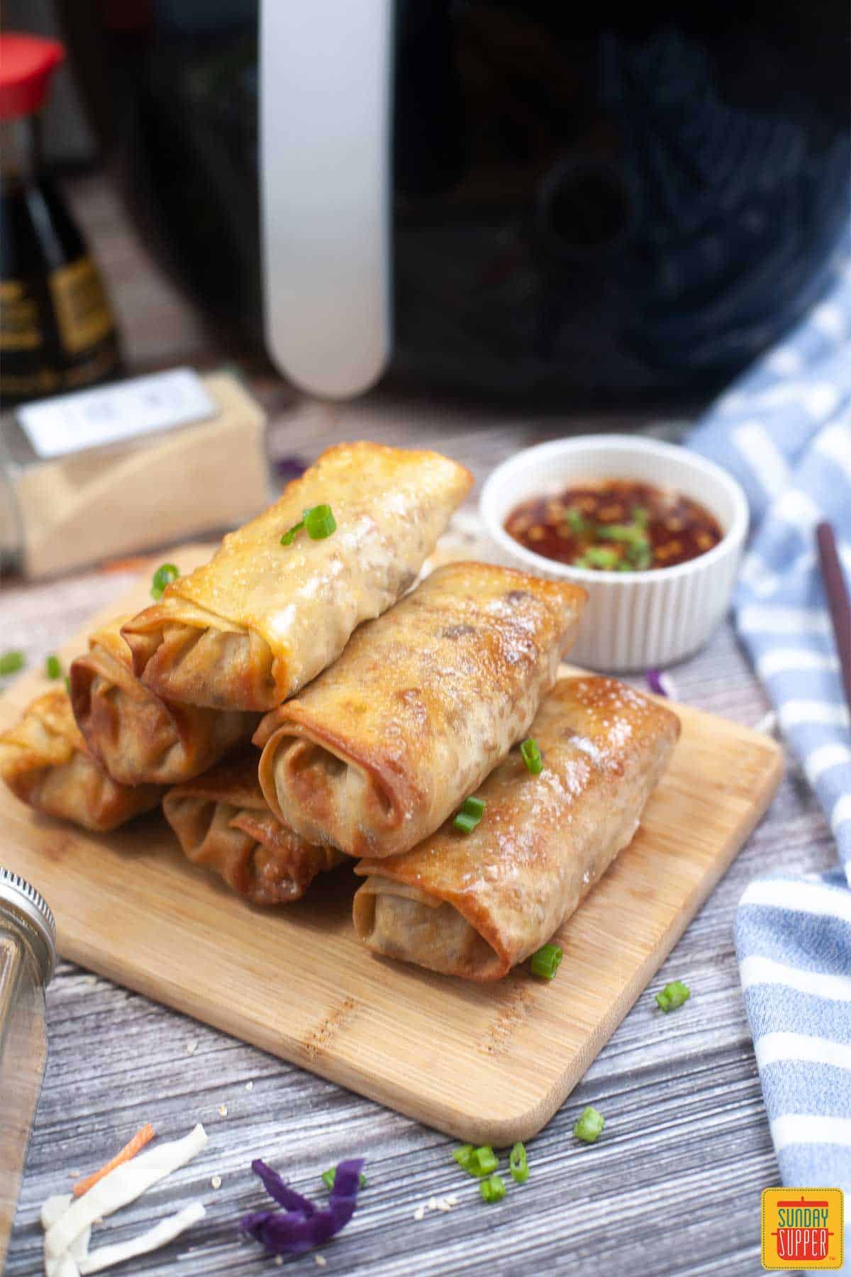 air fryer egg rolls stacked on a wooden serving board