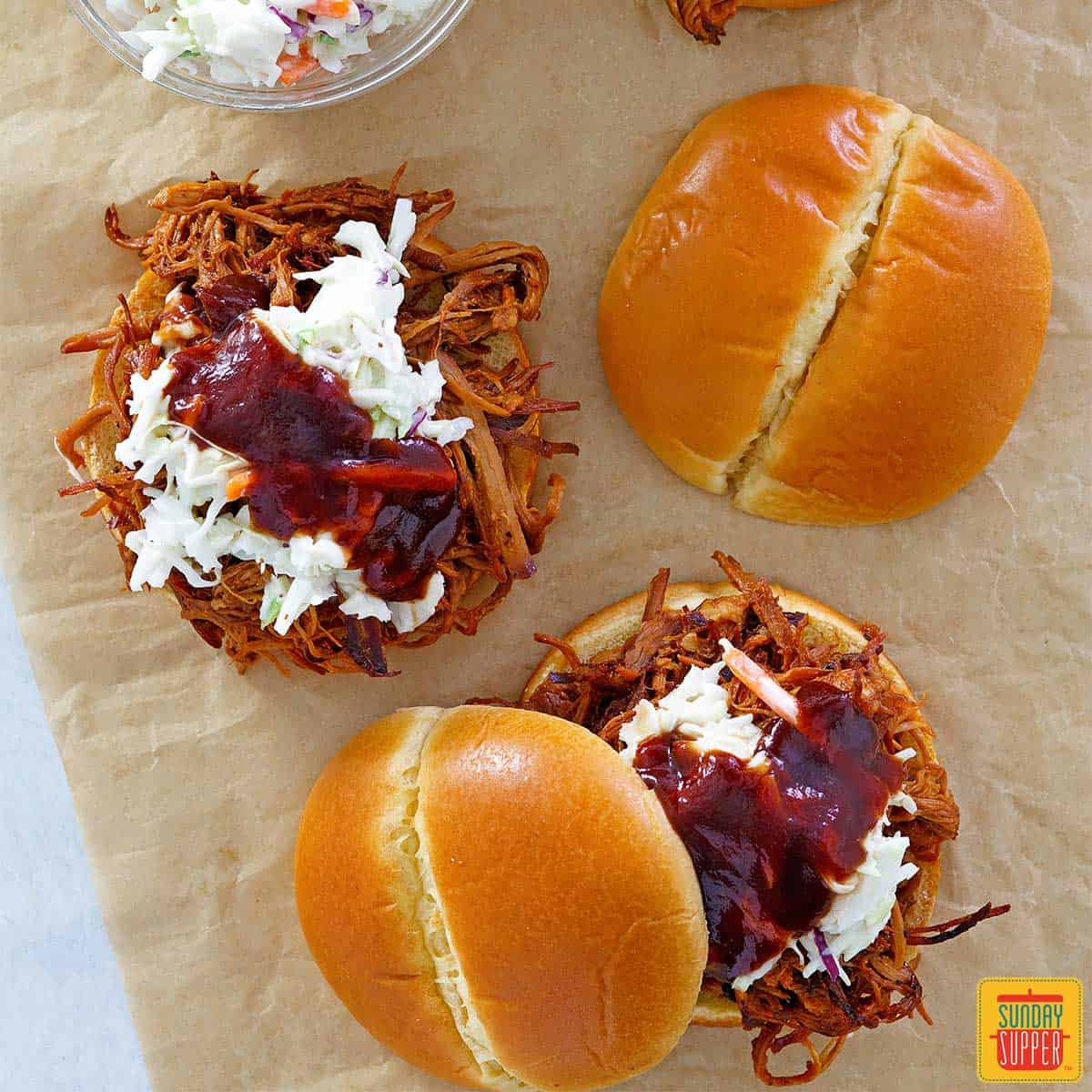 two slow cooker pulled pork sandwiches with buttery buns on parchment paper