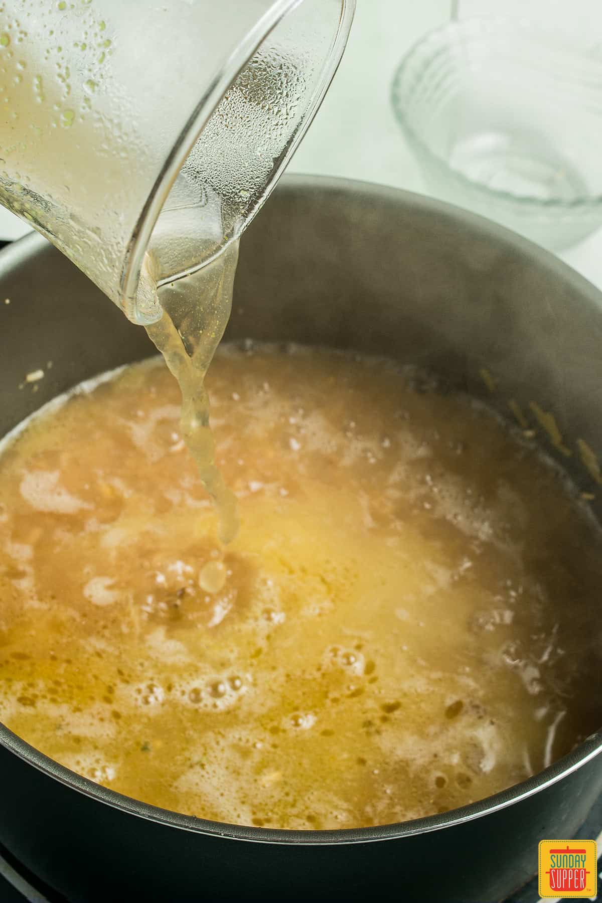 adding chicken stock to rice-a-roni in a pot