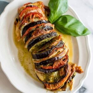 Sliced roasted eggplant on a white plate with fresh basil leaves