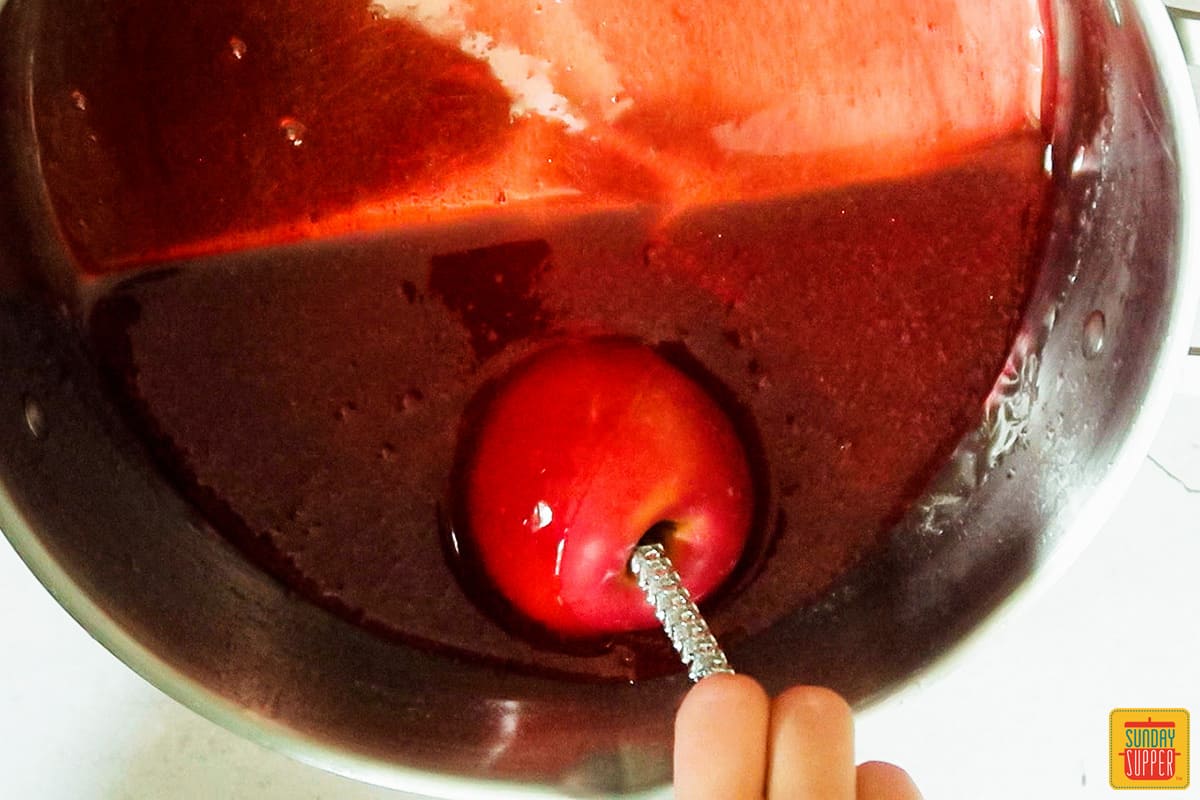 dipping apples into candy mixture for candied apples