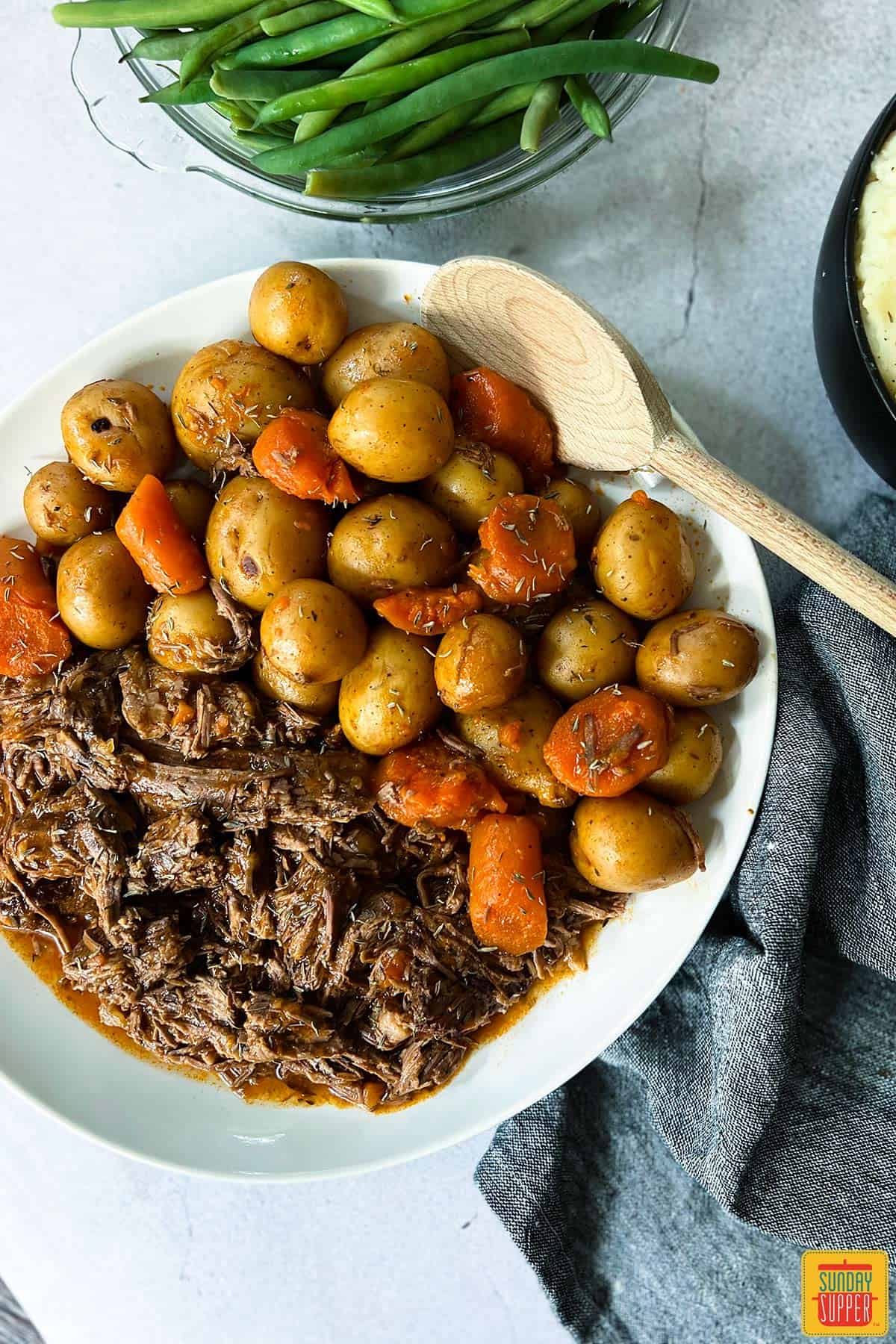instant pot chuck roast on a plate with a wooden spoon, potatoes, and carrots