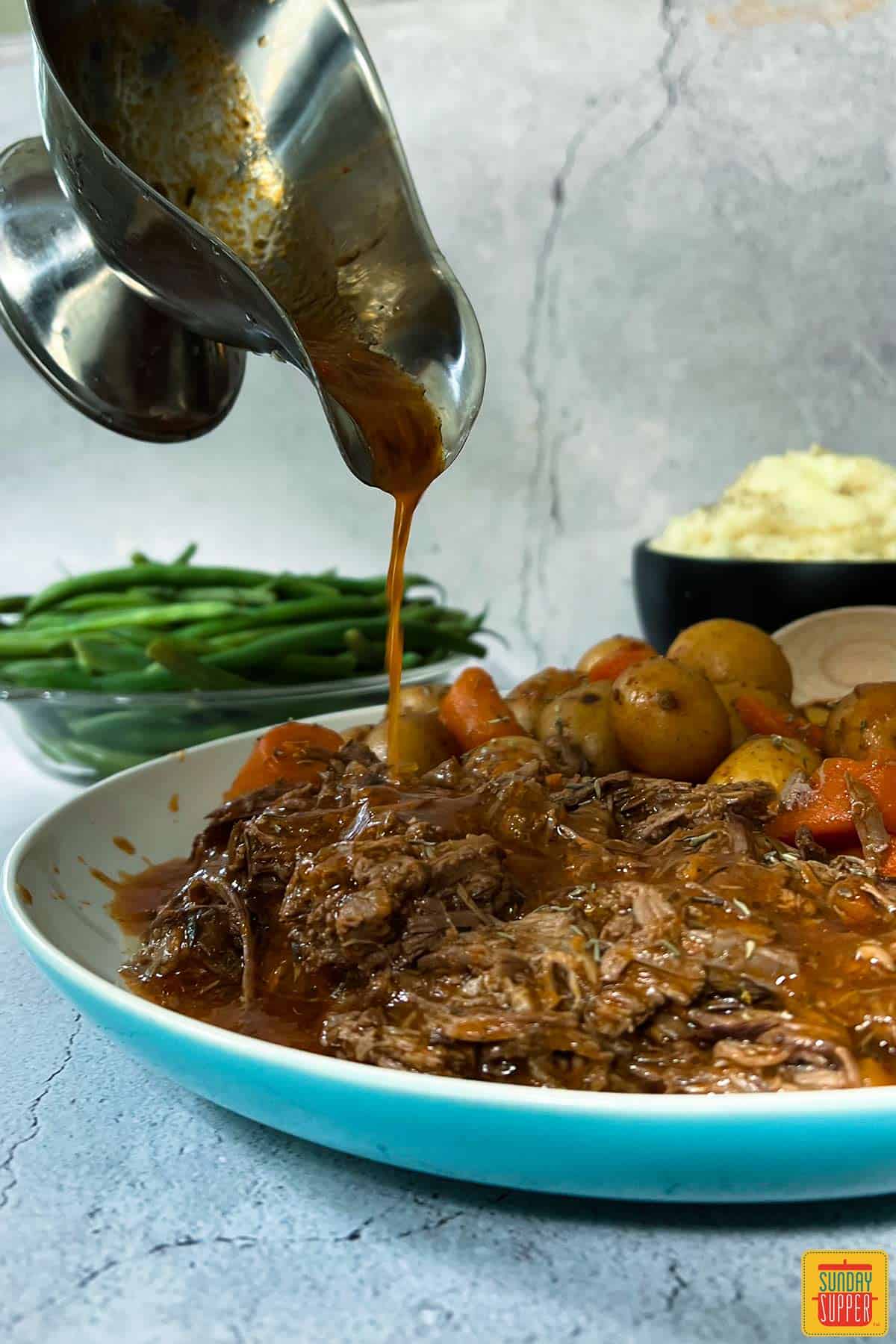 pouring gravy over instant pot chuck roast on a plate