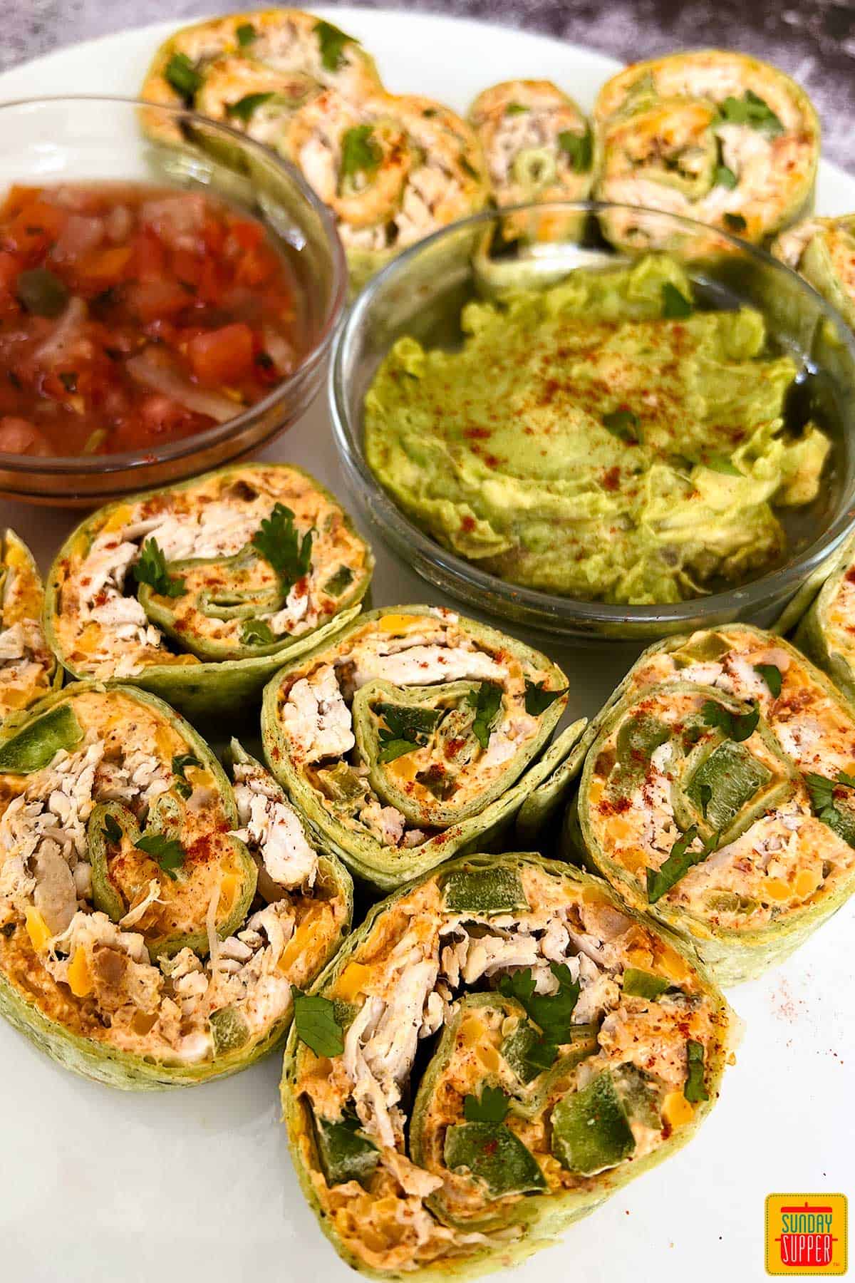 jalapeno popper pinwheels on a white plate with salsa and guacamole.