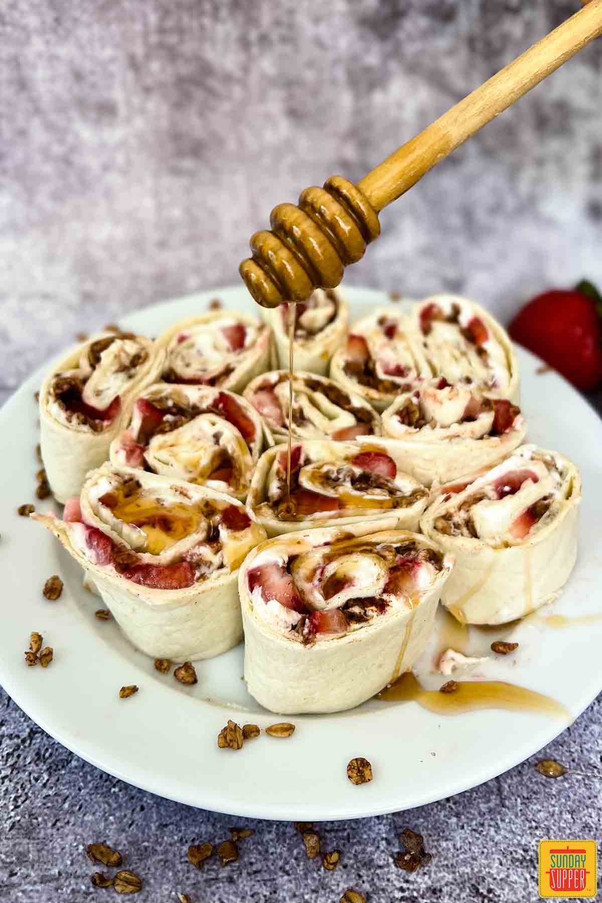 strawberry cream cheese pinwheel sandwiches on a plate with drizzled honey