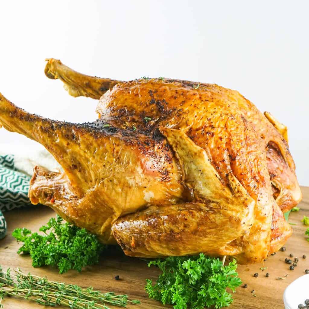 whole deep fried turkey on a wooden board next to herbs