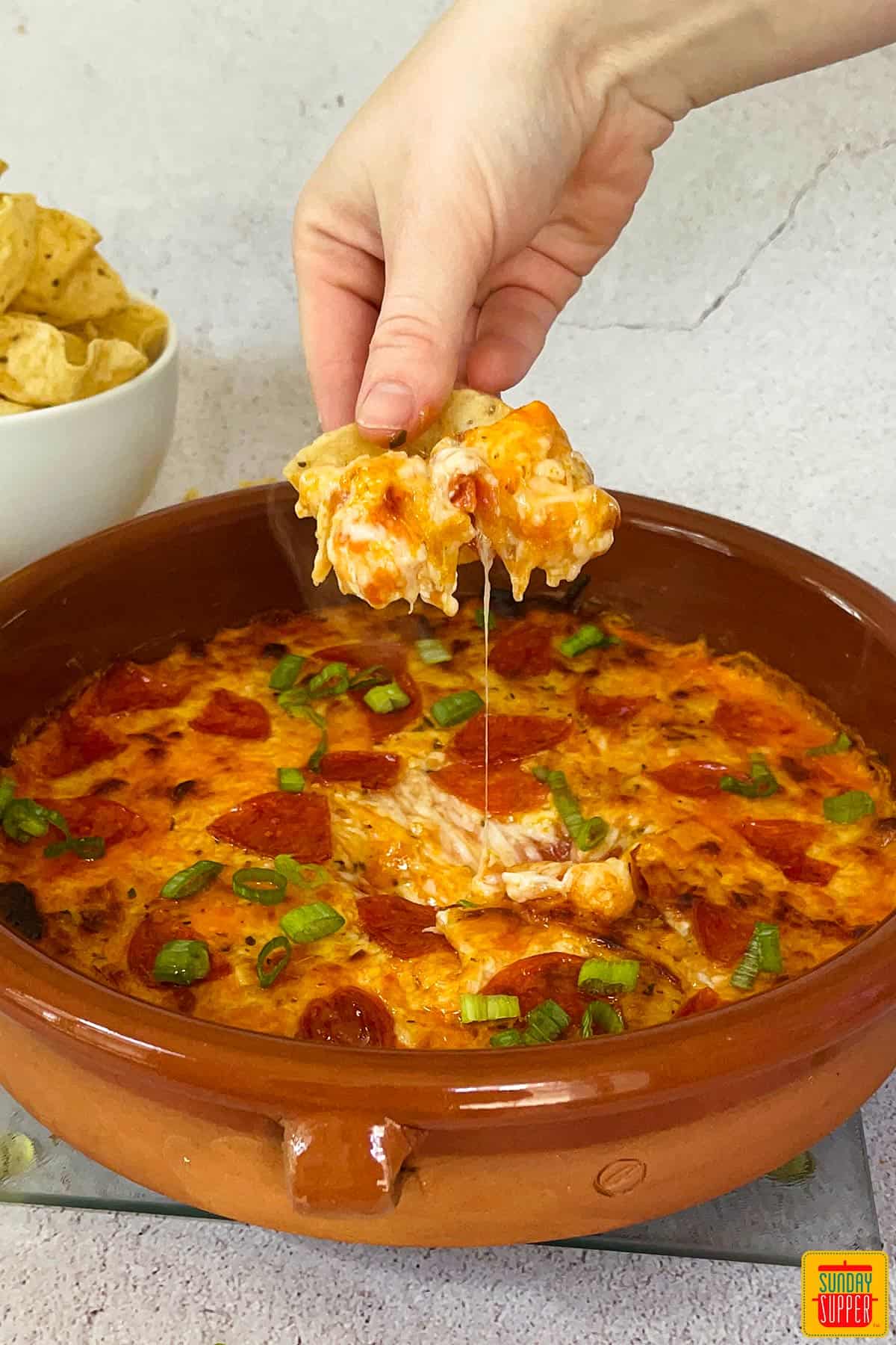 pizza dip in a brown baking dish being scooped by a chip