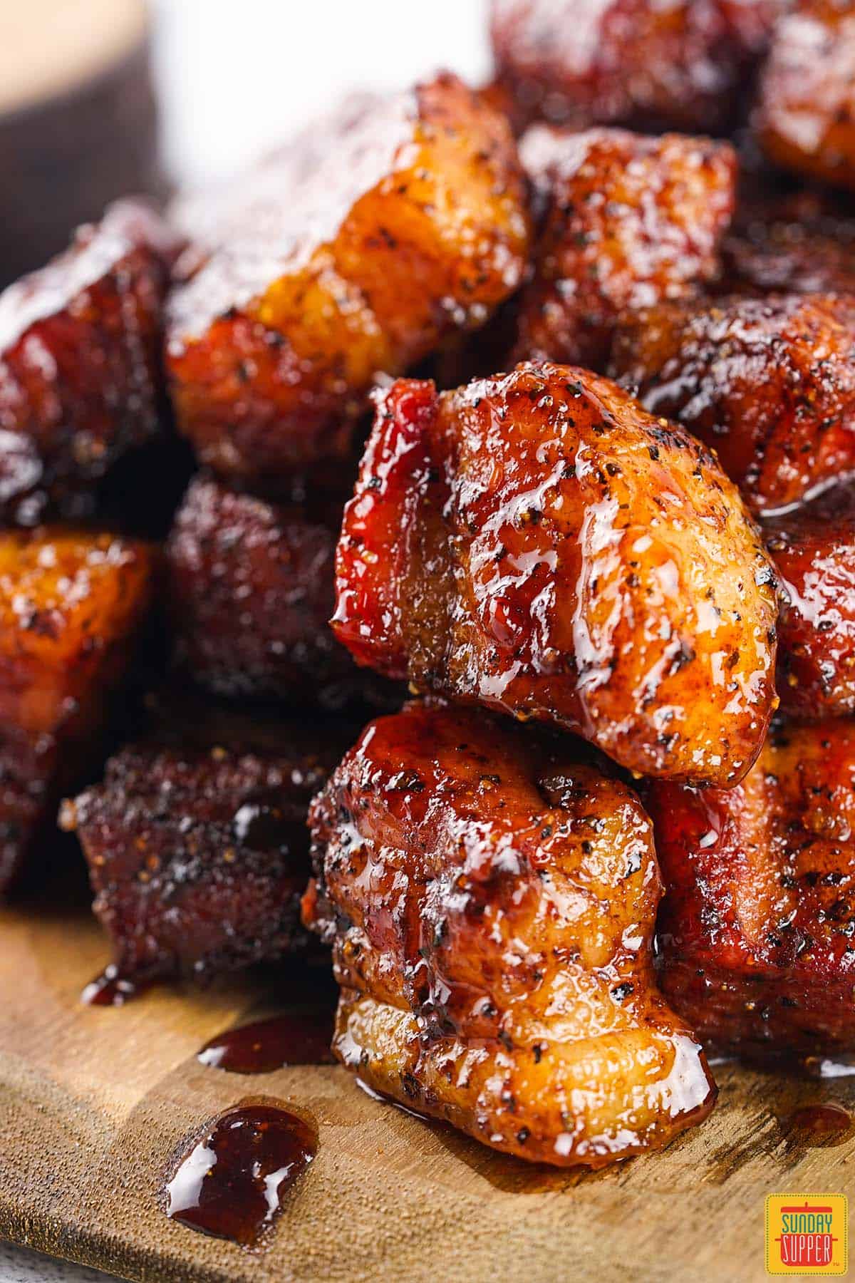 pork belly burnt ends stacked on top of each other on a wooden serving board with bbq sauce