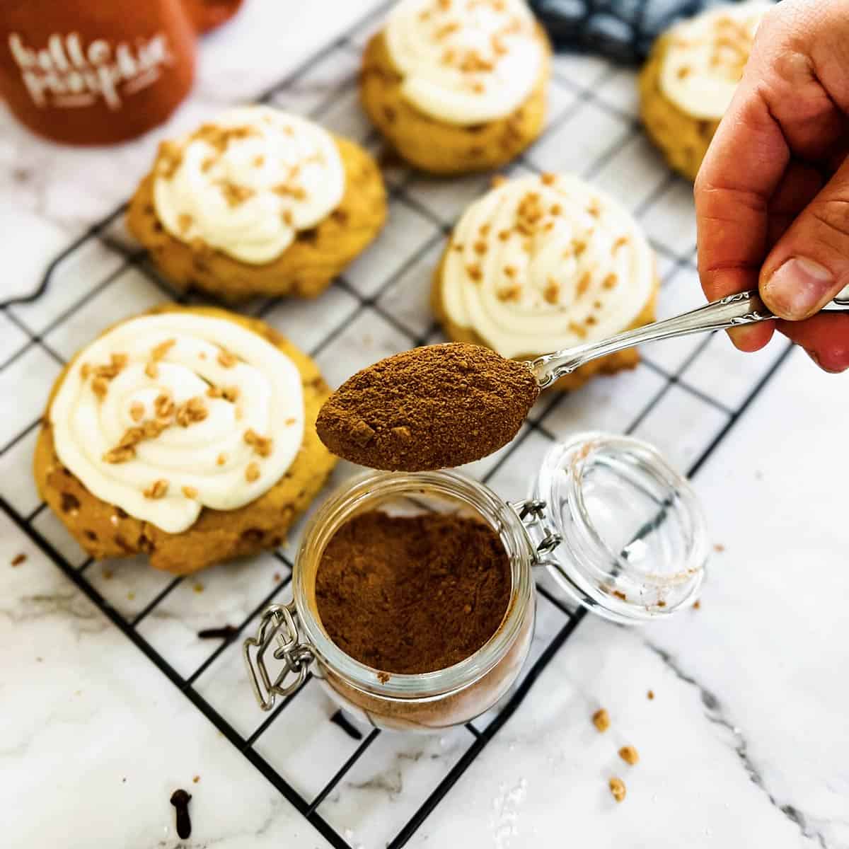 holding a spoon of pumpkin spice over a tray of pumpkin pie cookies with frosting