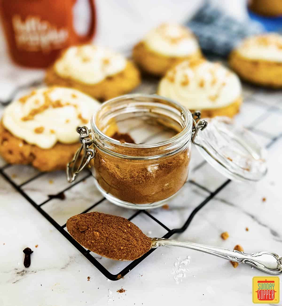 pumpkin pie spice in a jar next to a spoon of spice and pumpkin pie cookies