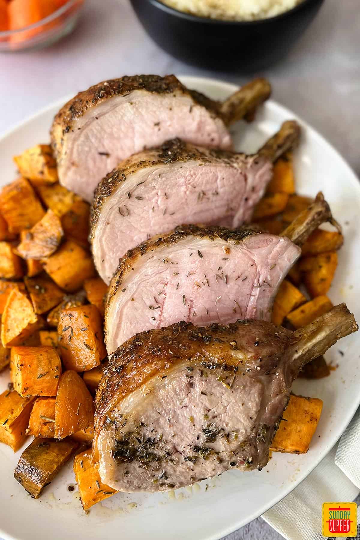 rack of pork sliced on a white plate with sweet potatoes under neath