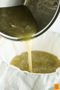 pouring turkey stock through a cheesecloth to strain it