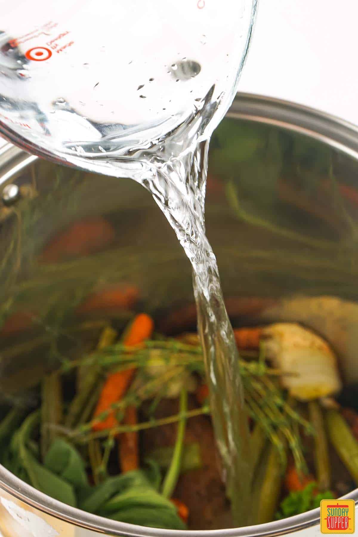 pouring water into the pot of veggies, herbs, and turkey