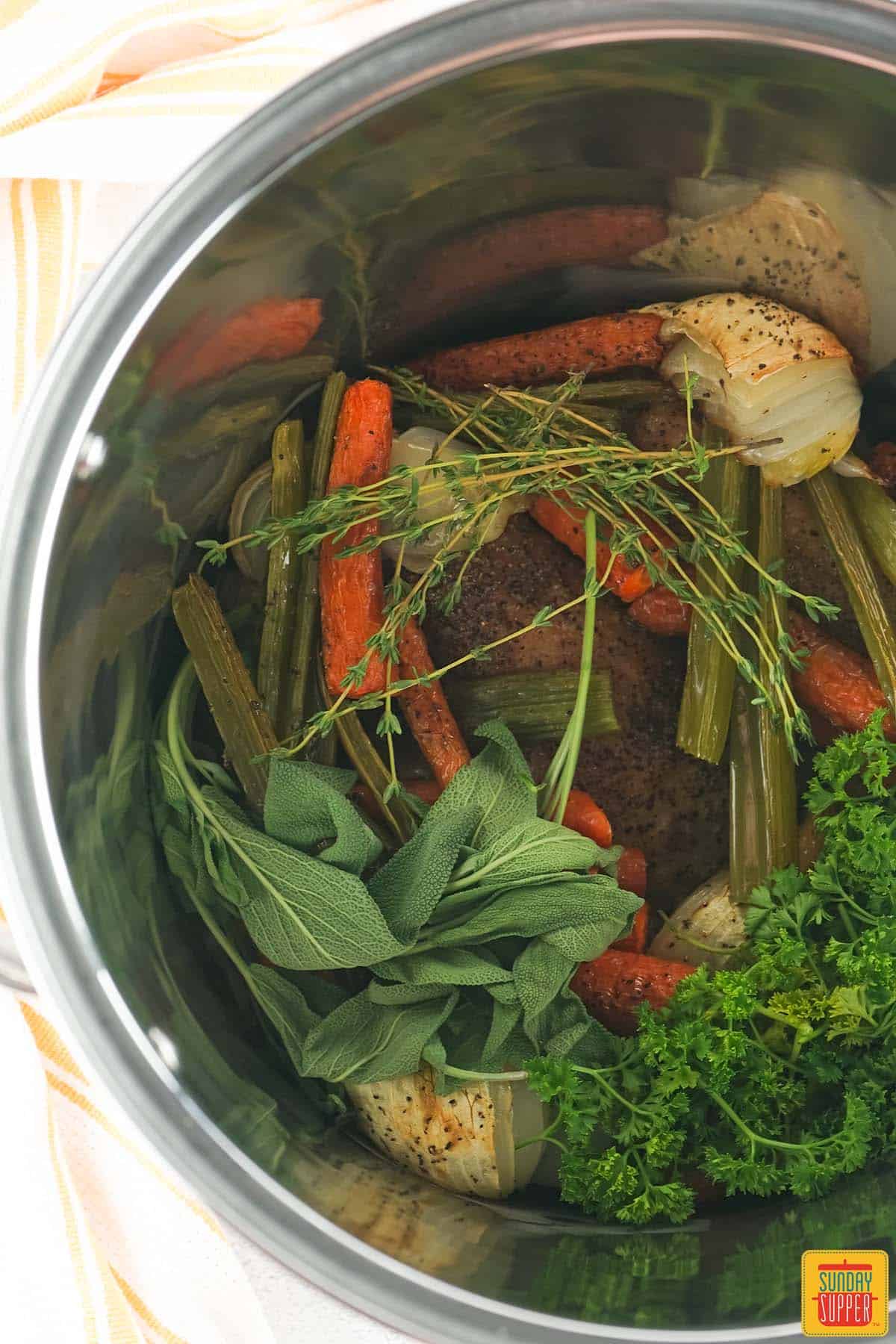 adding roasted veggies and herbs with turkey pieces to a pot