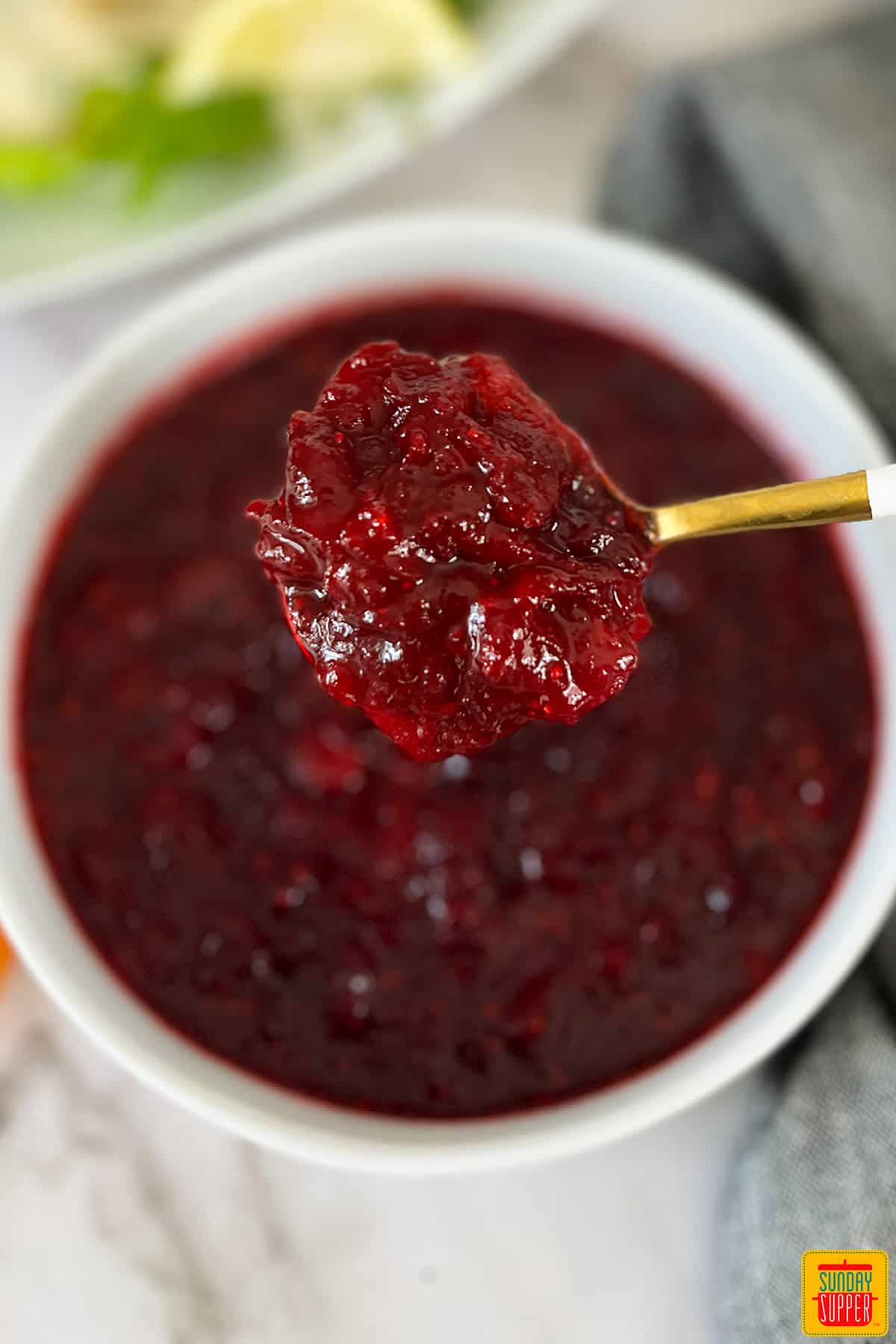 cranberry sauce in a white bowl with a white and gold spoon taking a spoonful