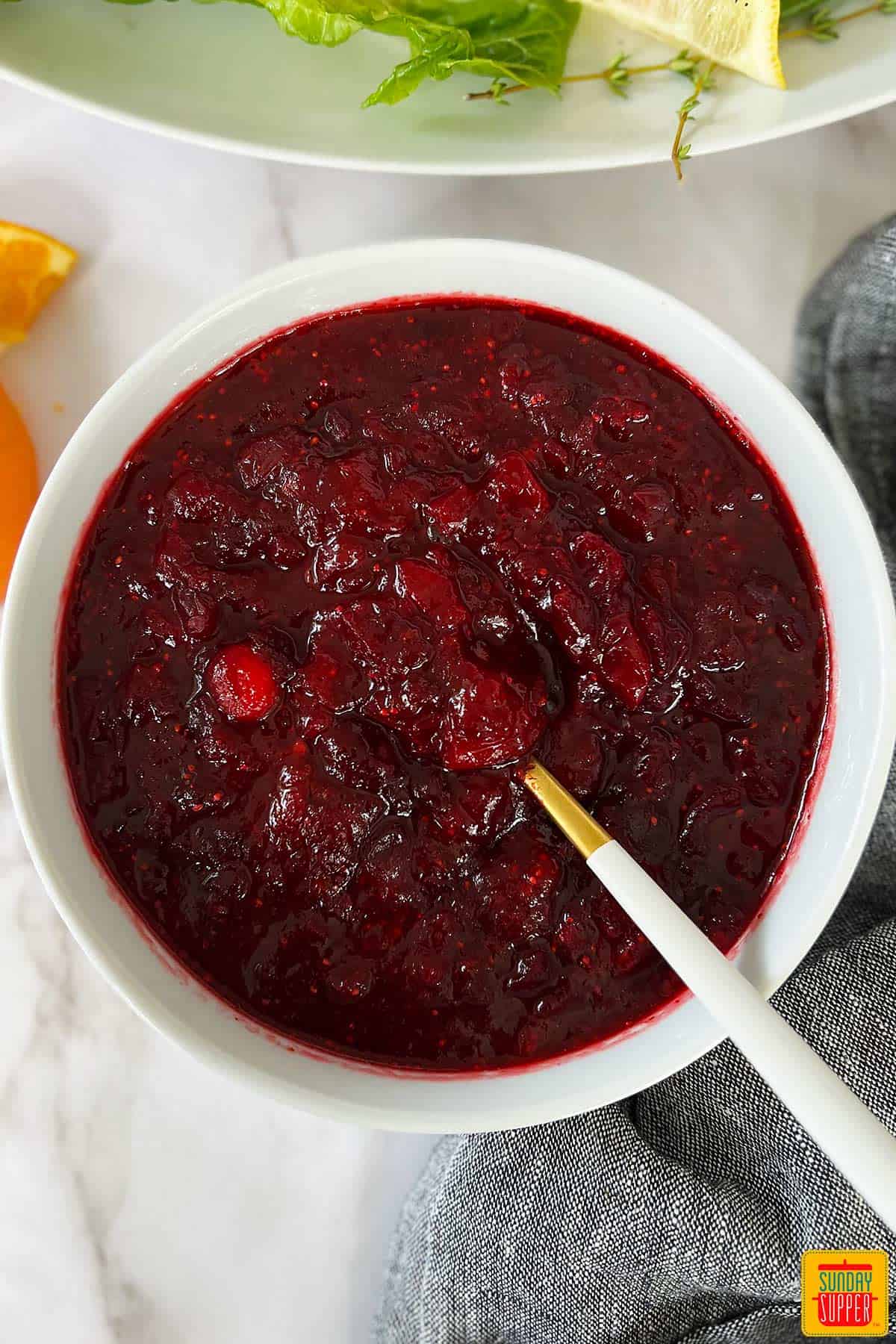 cranberry sauce in a white bowl with a white and gold spoon inside