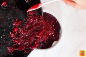 transferring cranberry sauce from the saucepan into a white dish