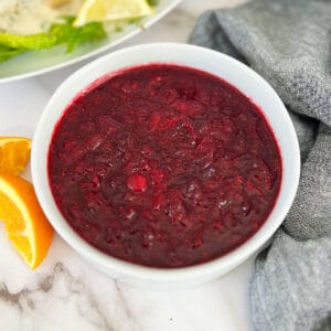 cranberry sauce in a white bowl with an orange next to the bowl