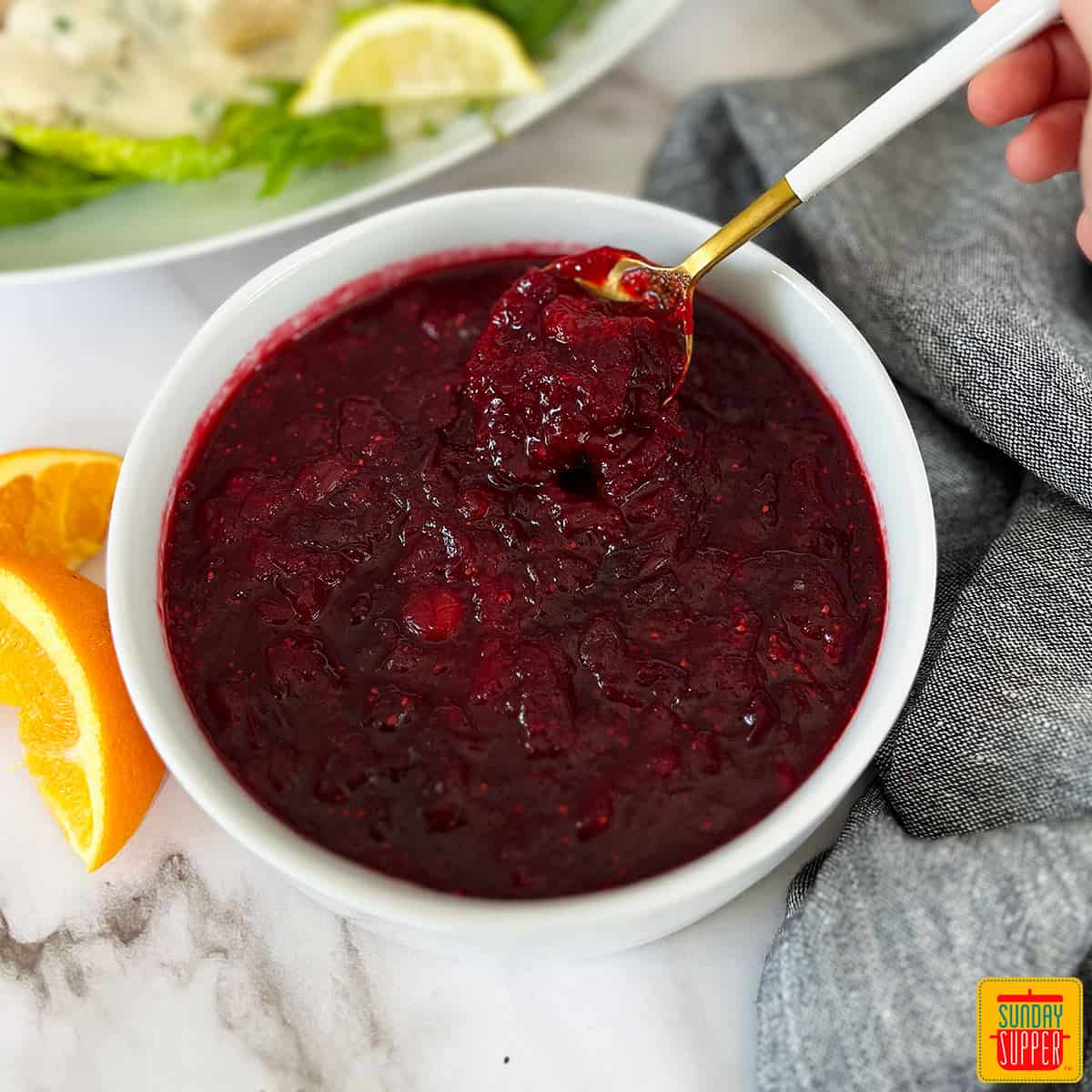 cranberry sauce in a white bowl with a white and gold spoon inside