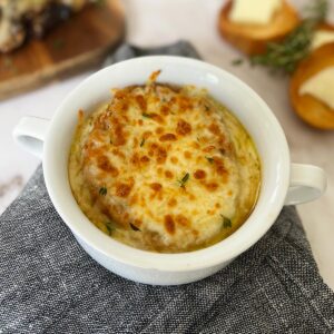 instant pot French onion soup in a white bowl on top of a grey napkin and bread in the background