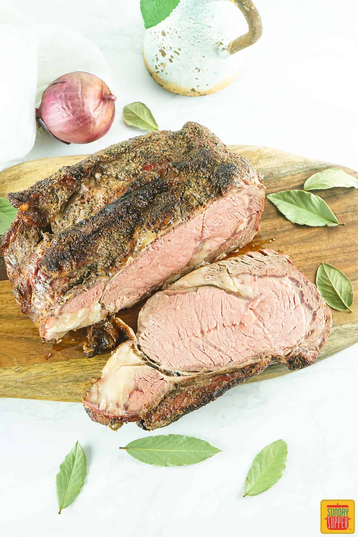 sliced smoked prime rib on a cutting board with herbs and an onion