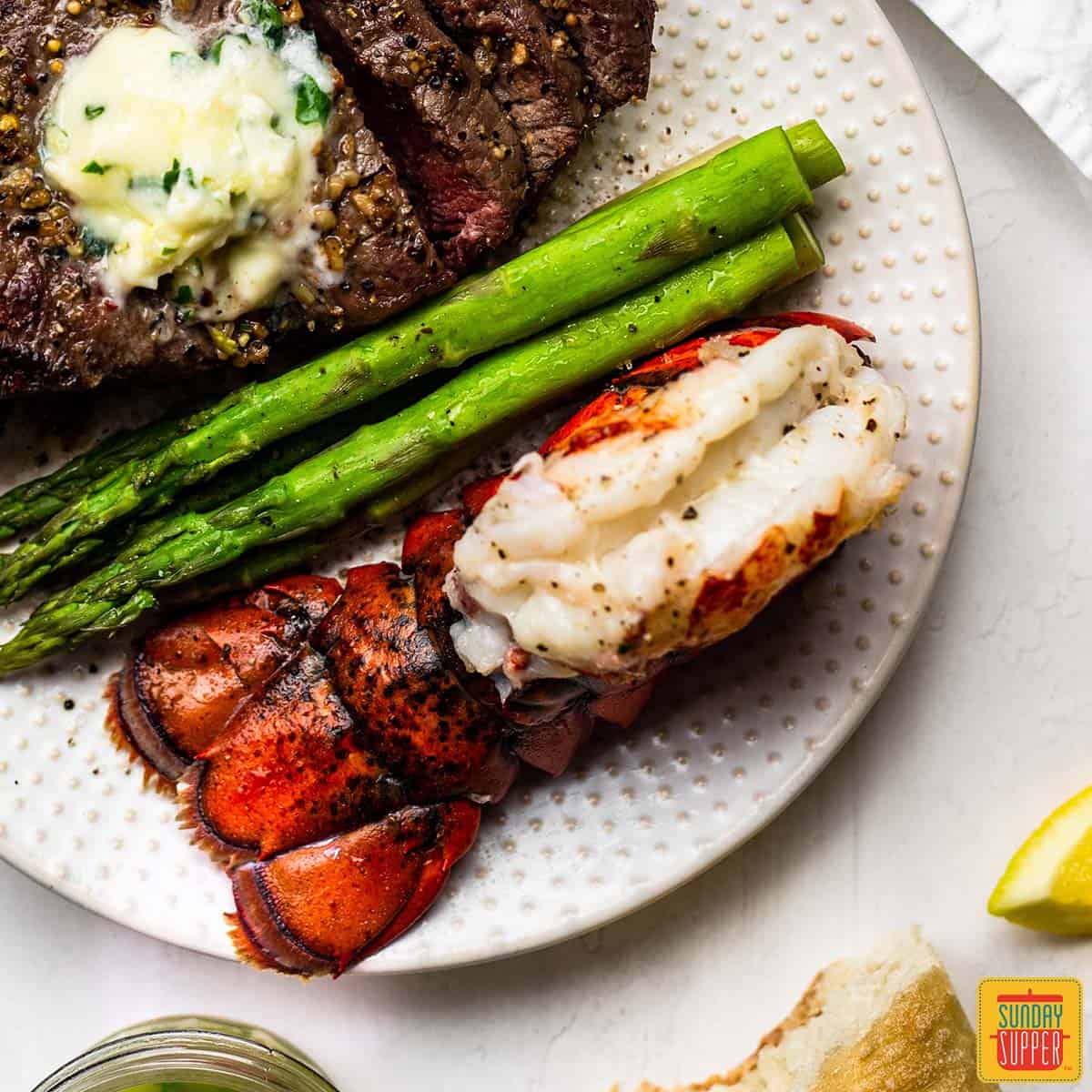 Air fryer lobster tail on a plate with asparagus and steak