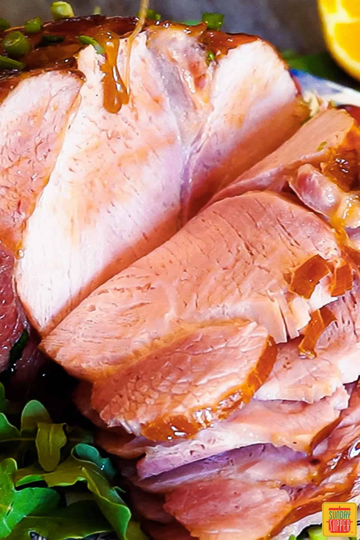 sliced baked ham on a dish, with honey glaze being poured from above