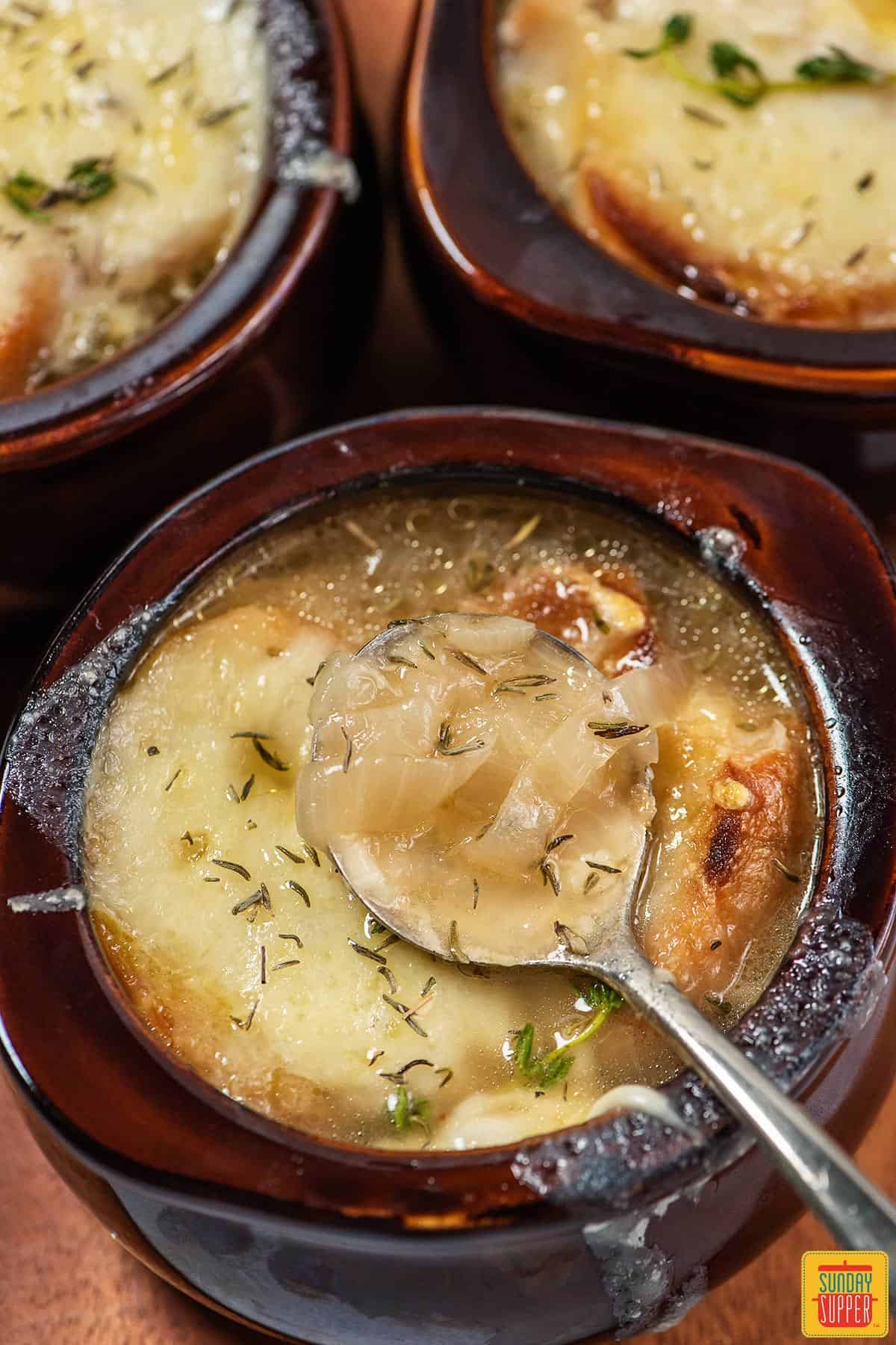 3 bowls of French onion soup in a brown bowl with a metal spoon inside