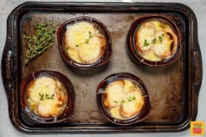 4 broiled and melty bowls of French onion soup on a baking tray