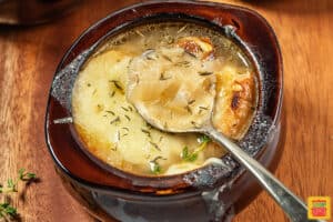 French onion soup in a brown bowl with a metal spoon inside
