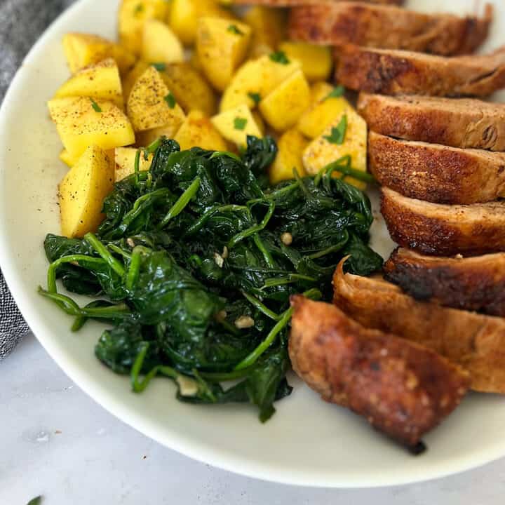 sautéed spinach on a white plate with pork and potatoes