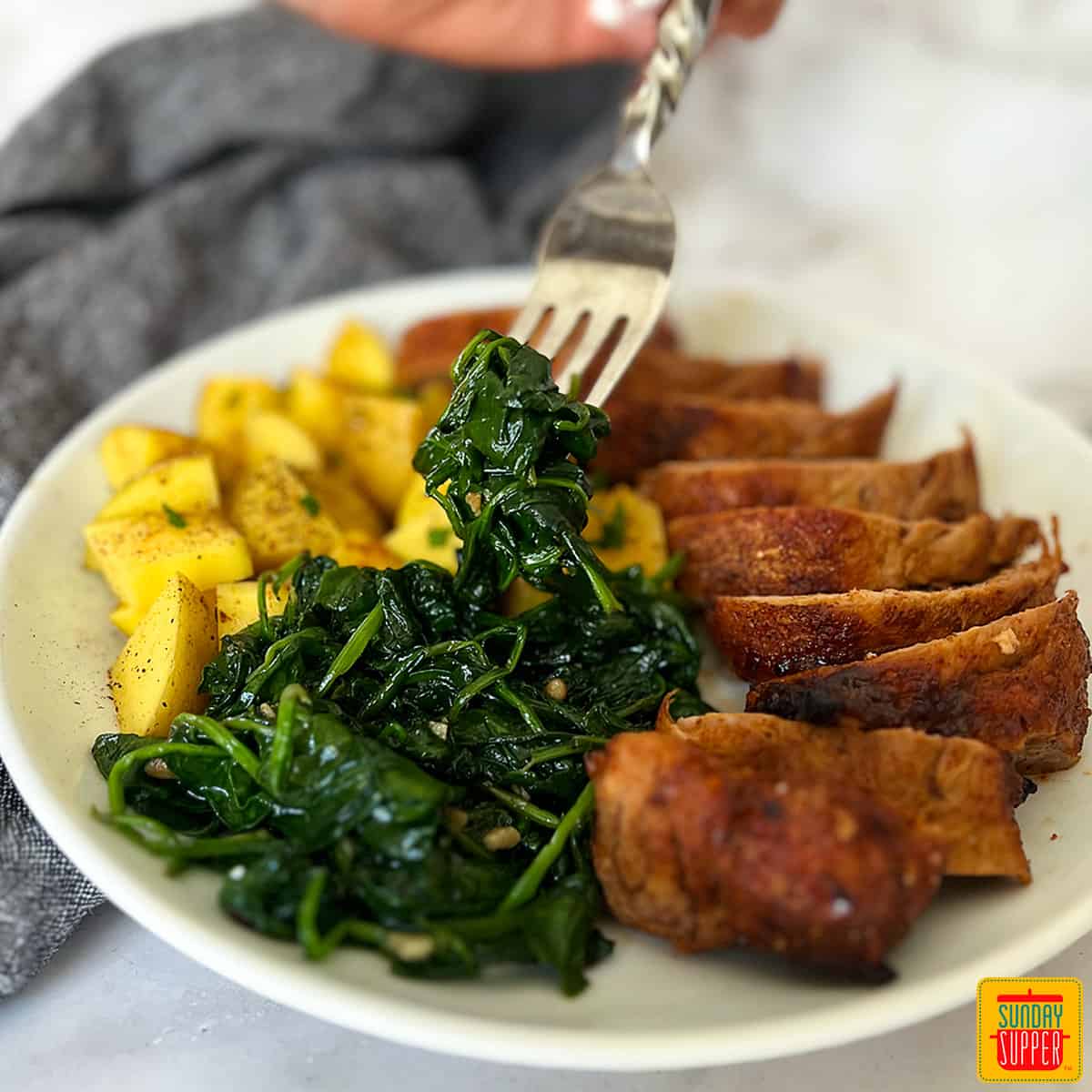 sautéed spinach on a white plate with pork and potatoes