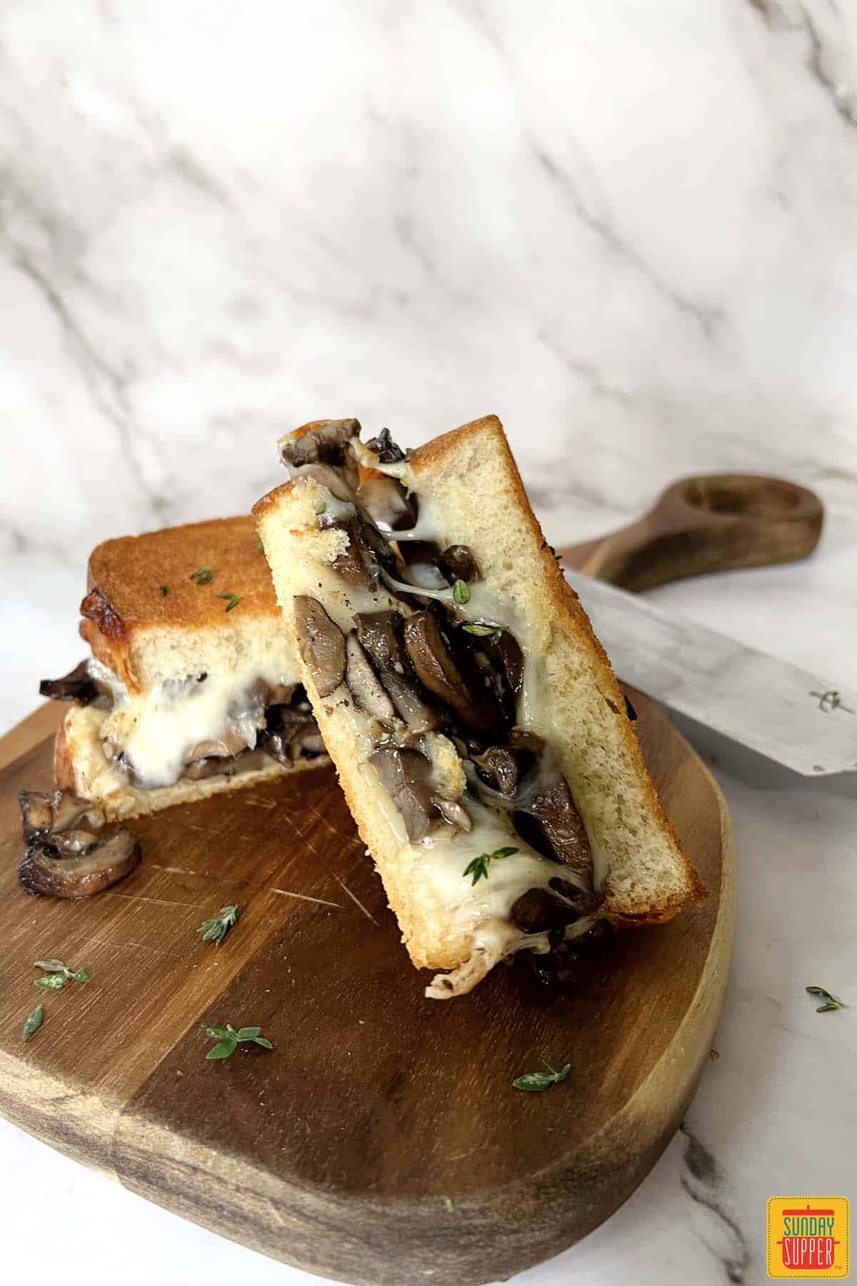 two halves of a mushroom grilled cheese on a cutting board